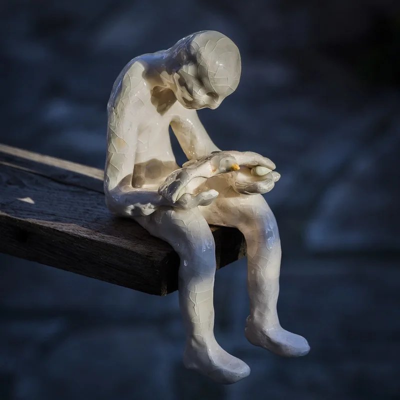 Crackle-glazed ceramic sculpture of a seated boy holding a bird