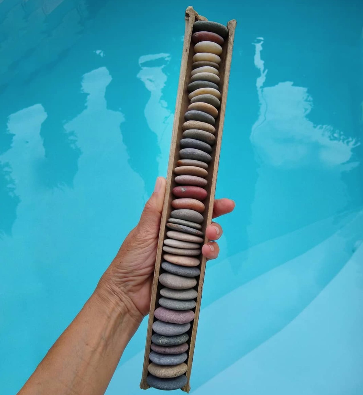 Wooden tray of flat beach pebbles arranged by colour