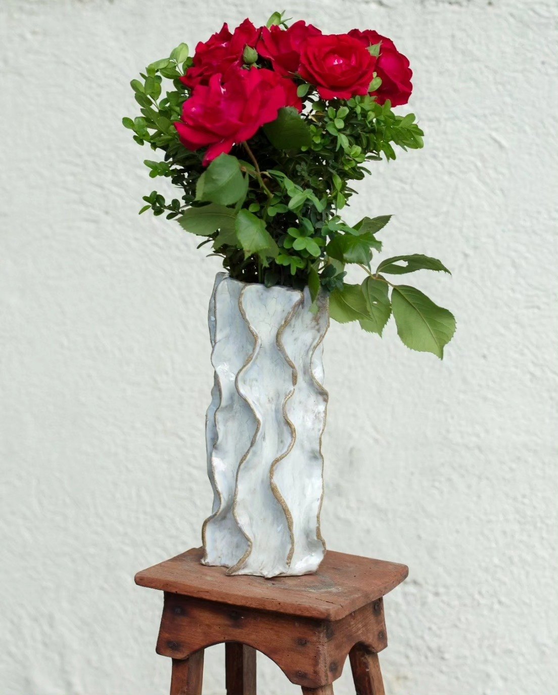 Wavy white ceramic vase holding red roses and greenery