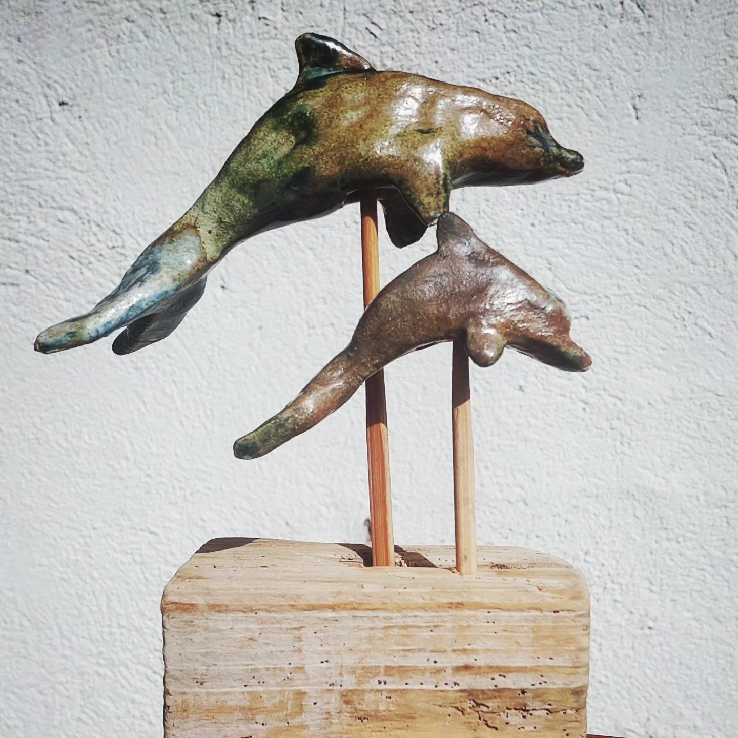 Bronze-glazed ceramic sculpture of two leaping dolphins on a wooden base